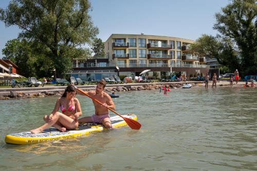 a man and a woman sitting on a paddle board in the water at Hotel Azur Siofok in Siófok
