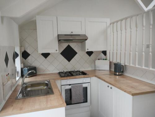 uma pequena cozinha com armários brancos e um lavatório em Cwtch Cottage em Rhondda