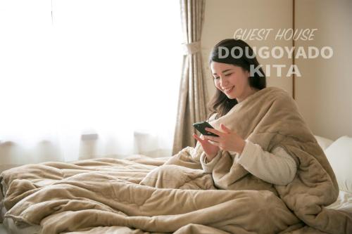 a woman laying in bed looking at a cell phone at GUEST HOUSE DOUGOYADO KITA - Vacation STAY 14923 in Matsuyama