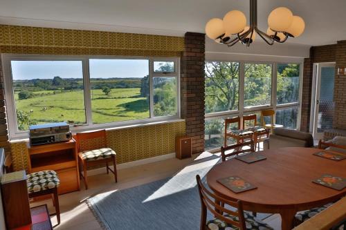 a living room with a table and chairs and windows at Pant Golau - The Seventies House in Llanbedr