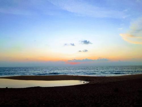 a sunset over the ocean with a puddle on the beach at BAWANS VILLA Holiday Home for Family or Group in Hikkaduwa