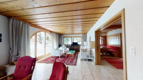 a living room with wooden ceilings and red chairs at Greina in Celerina