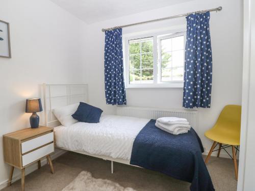 a bedroom with a bed with blue curtains and a window at Cynefin in Llangefni
