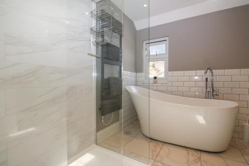 uma casa de banho branca com uma banheira e uma cabina de duche em vidro. em Garden Cottage em Farnham
