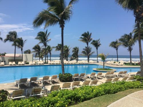uma piscina com cadeiras e palmeiras e o oceano em Departamento Playa Punta Diamante em Acapulco