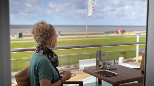 a woman sitting at a table looking out a window at the ocean at Hotel Strandperle in Cuxhaven