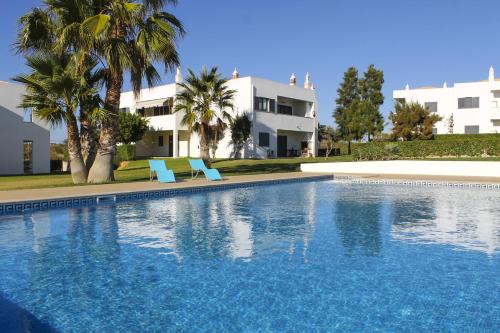 una piscina con 2 sillas azules y un edificio en Condominio Vilita, T1-Lt-5,F Pera-Silves en Pêra