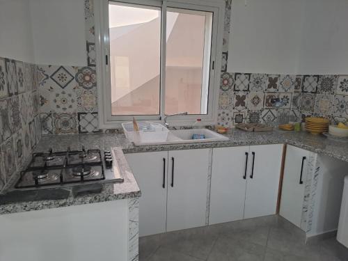 Dar El Yasmine 2 في Kerkouene: مطبخ بدولاب بيضاء ومغسلة ونافذة
