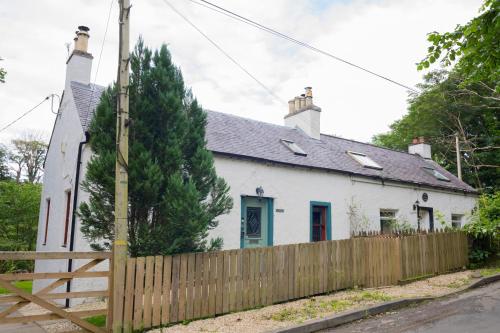 a white house with a wooden fence at Tig Cottage - a rural, quirky, pet friendly 2 bedroom cottage near Ballantrae in Ballantrae