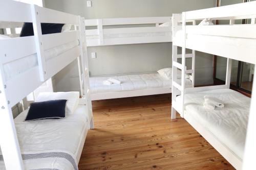 a room with white bunk beds with wooden floors at A Beira Hostel in Aveiro