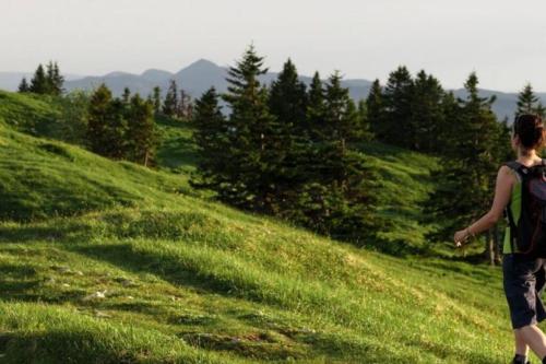 a woman walking on a grassy hill with a backpack at GITE La fromagerie Haut Jura in La Mouille