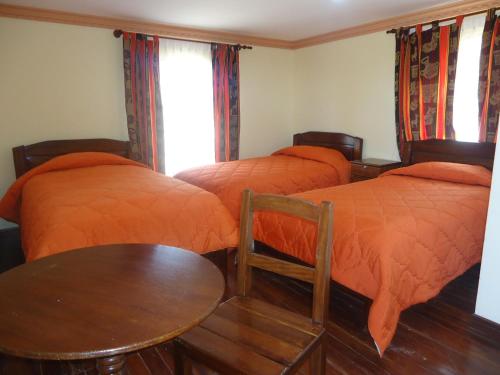 2 letti con coperte arancioni in una stanza con tavolo di Hostal del Sol Isla del Sol a Isla de Sol