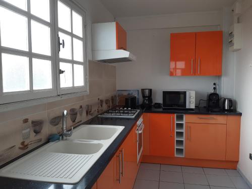 una cocina con armarios naranjas, fregadero y ventana en Les ptits flamboyants, en Basse-Terre