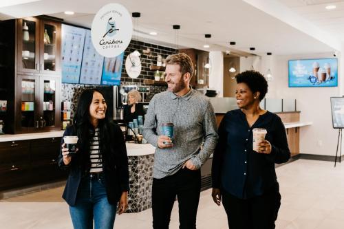 three people standing in a coffee shop holding drinks at Holiday Inn & Suites St. Cloud by IHG in Saint Cloud