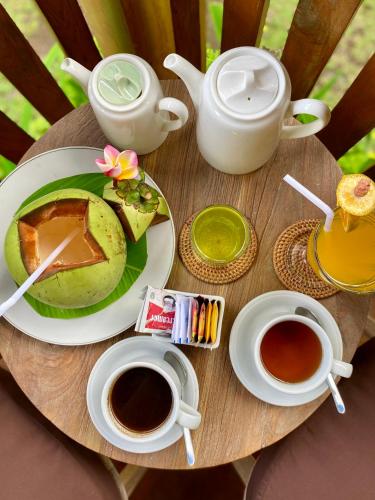 a table with a plate of food and cups of coffee at The Banana’s Kumbe Villa in Tampaksiring