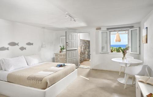 a white bedroom with a bed and a table and a window at VLIA MAR Myconian Residences in Kalafatis