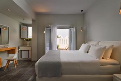 a bedroom with a large white bed and a desk at Meltemi Village Hotel in Perissa
