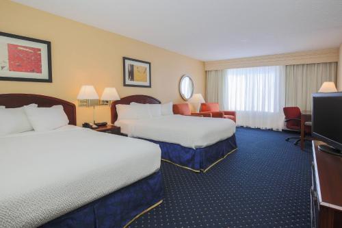 a hotel room with two beds and a flat screen tv at Courtyard by Marriott Flint Grand Blanc in Flint