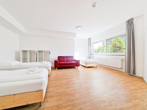 a white room with two beds and a red chair at Tolstov Apartments - 1 or 3 Room Apartments with Balcony - 20 Min Messe DUS & Airport DUS in Meerbusch