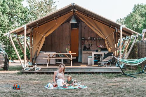 una mujer y dos niños sentados frente a una tienda en Glamping Holten luxe safaritent 1, en Holten