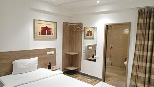a bedroom with a bed and a bathroom with a shower at Sapphero Akshar Inn- Jamnagar in Jamnagar