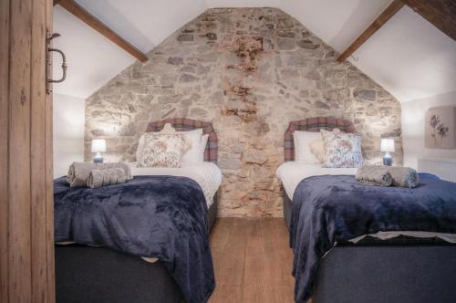 two beds in a room with a stone wall at The Lodge - 2 Bedroom Cottage - Princes Gate in Ludchurch