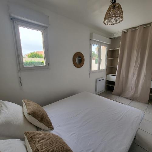 a white bedroom with a large bed and a window at Bel appartement avec jardin de 30m2 , climatisé avec parking et arrivée autonome in Cabestany