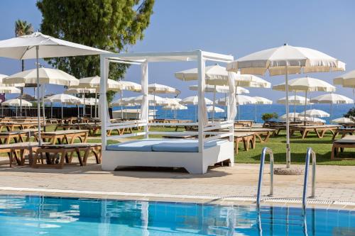 a pool with tables and white umbrellas next to a pool at Capo Bay Hotel in Protaras