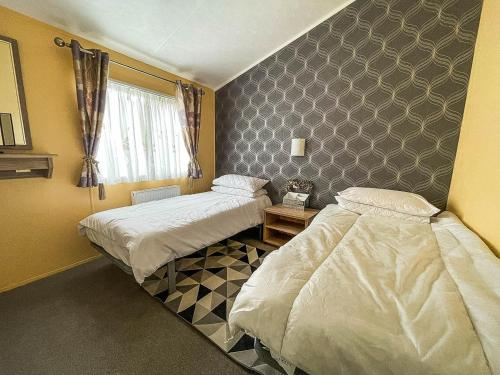 1 dormitorio con 2 camas y una pared con ventana en Stunning Lodge With Decking At Oaklands Holiday Park In Essex Ref 39017rw en Clacton-on-Sea