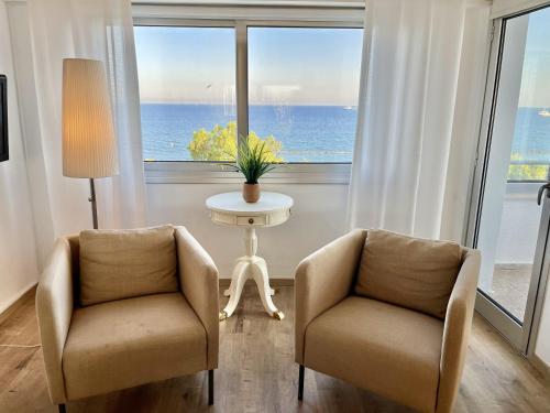 2 stoelen en een tafel in een kamer met een groot raam bij Seaview Beach Apartment Dasoudi in Limassol