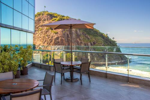 a table with an umbrella on a balcony overlooking the ocean at Arena Leme Hotel in Rio de Janeiro