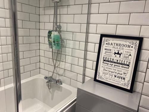a white tiled bathroom with a sign next to a bath tub at Suburban 2-bed, entire home, free parking, Maidstone, Kent UK in Boxley