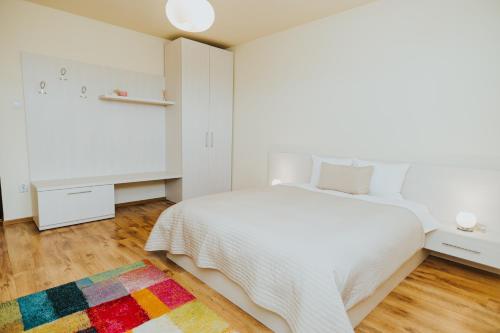 a white bedroom with a white bed and a colorful rug at Camelia's cozy place in Baia Mare