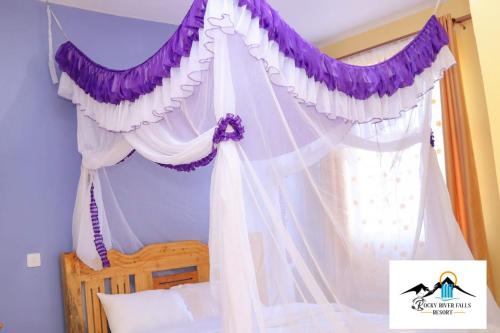 a bedroom with a canopy with purple and white curtains at Rocky river falls resort in Thika