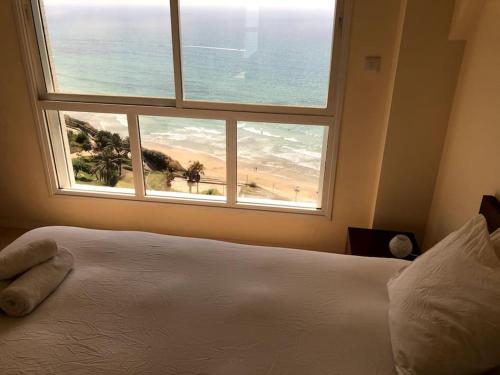 een slaapkamer met een bed en een raam met een strand bij Nitza Seaview Apartments in Netanya