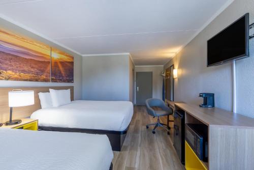 a hotel room with two beds and a desk with a tv at Days Inn & Suites by Wyndham Fort Bragg/Cross Creek Mall in Fayetteville