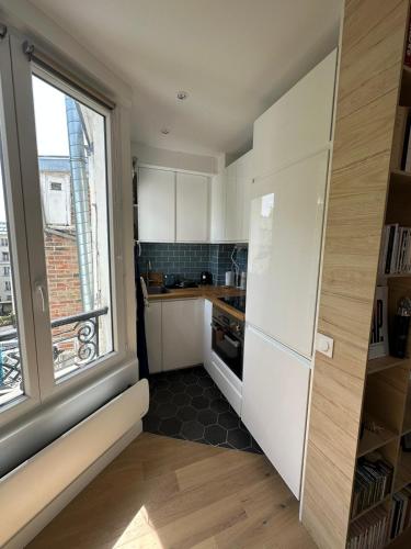 une cuisine avec des placards blancs et une grande fenêtre dans l'établissement Studio au calme à deux pas du sacré coeur, à Paris