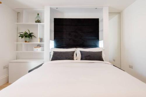 a bedroom with a large white bed with a black headboard at Well-Positioned Studio Flat in London