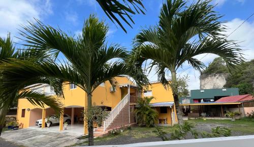 una casa amarilla con palmeras delante en Vacances chez HélèneB, en Sainte-Anne