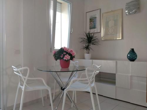 uma mesa de vidro com cadeiras brancas e um vaso com flores em Appartamento Orchidea em Rimini