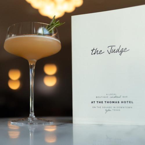 a cocktail in a glass next to a book at The Thomas Hotel - Premium Suite Main Level in Tyler