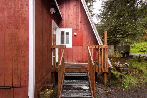 a red house with two wooden chairs on the side of it at THE SHORELINE CABIN in Kodiak
