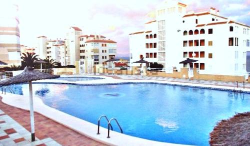 een groot blauw zwembad met gebouwen op de achtergrond bij Costamar playa arenales del sol in Arenales del Sol