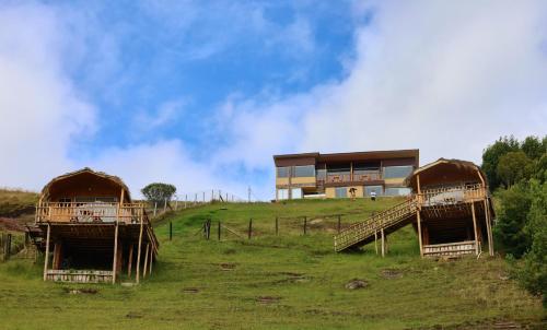 zwei Hütten auf einem Hügel vor einem Gebäude in der Unterkunft BluGlamp PlayaBlanca in Boyacá