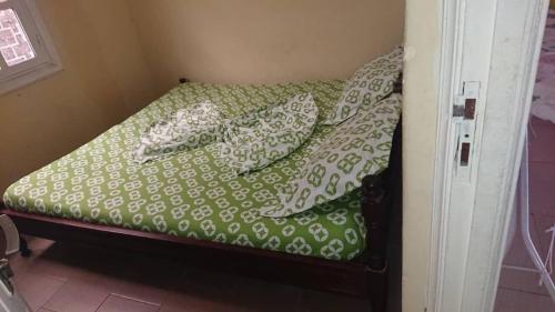 - un petit lit avec des draps et des oreillers verts et blancs dans l'établissement AUBERGE-NGOMSON, à Brazzaville