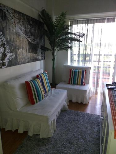 uma sala de estar com dois sofás brancos e uma palmeira em Beautiful condo with WIFI and pool near Nuvali em Cavite
