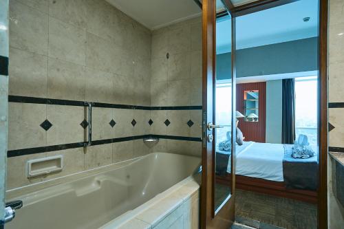 a bathroom with a bath tub and a bedroom at Horison Ultima Menteng Jakarta in Jakarta
