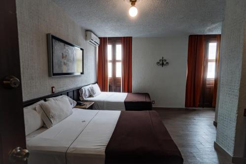 a hotel room with two beds and two windows at Hotel Don Quijote Plaza - Guadalajara Centro Historico in Guadalajara