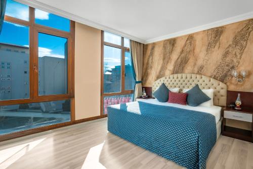 a bedroom with a bed with blue sheets and windows at GRAND ANİ HOTEL in Kars