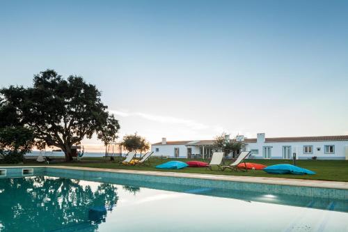 a swimming pool with two lawn chairs and a house at Pe no Monte in São Teotónio